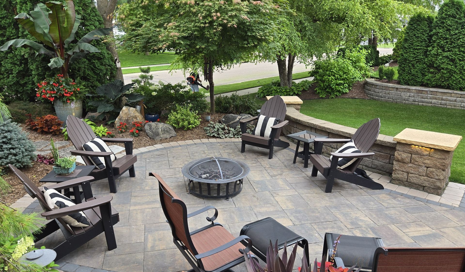 Fire pit patio with Adirondack chairs, brick pavers, and landscaping.