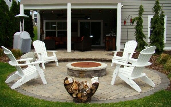 White Adirondack chairs around a stone fire pit on a circular patio.