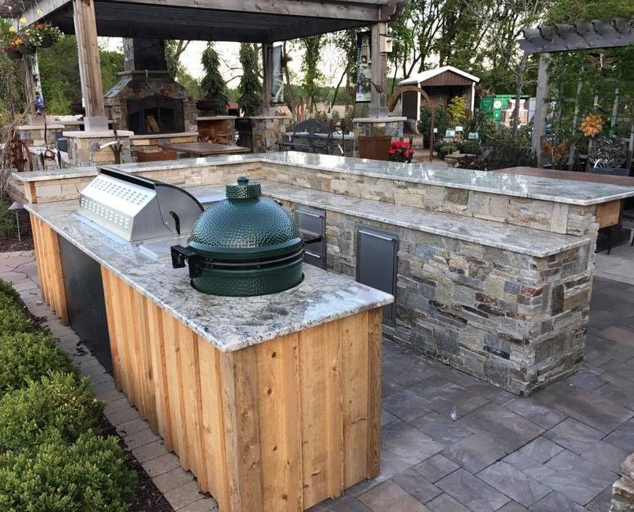 Outdoor kitchen with grill, Big Green Egg, and stone countertops under a pergola.