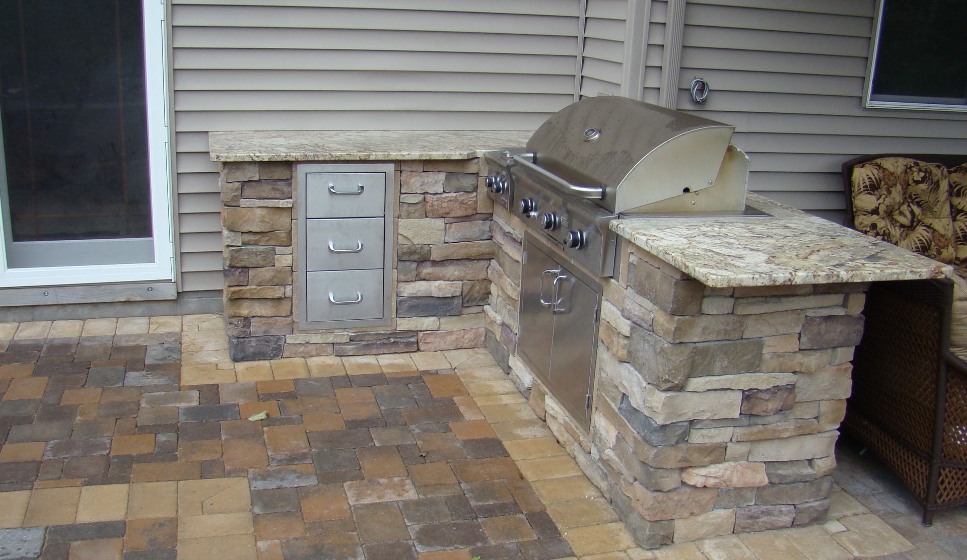 Outdoor kitchen with stone facing, stainless steel grill, storage drawers, and granite countertop.