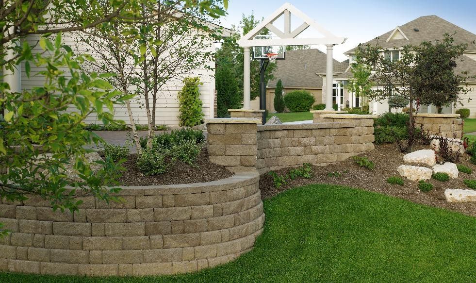 Landscaped yard with retaining walls, greenery, and a white pergola with basketball hoop.