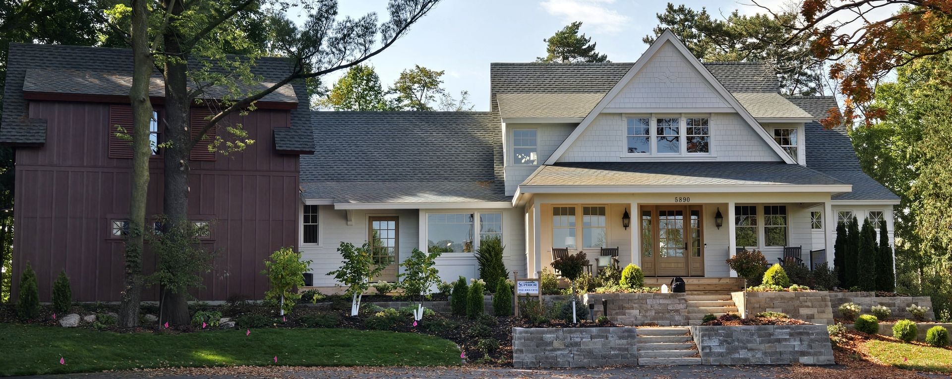 Large white house with a porch and a red shed on the left; stone wall and landscaping in front.