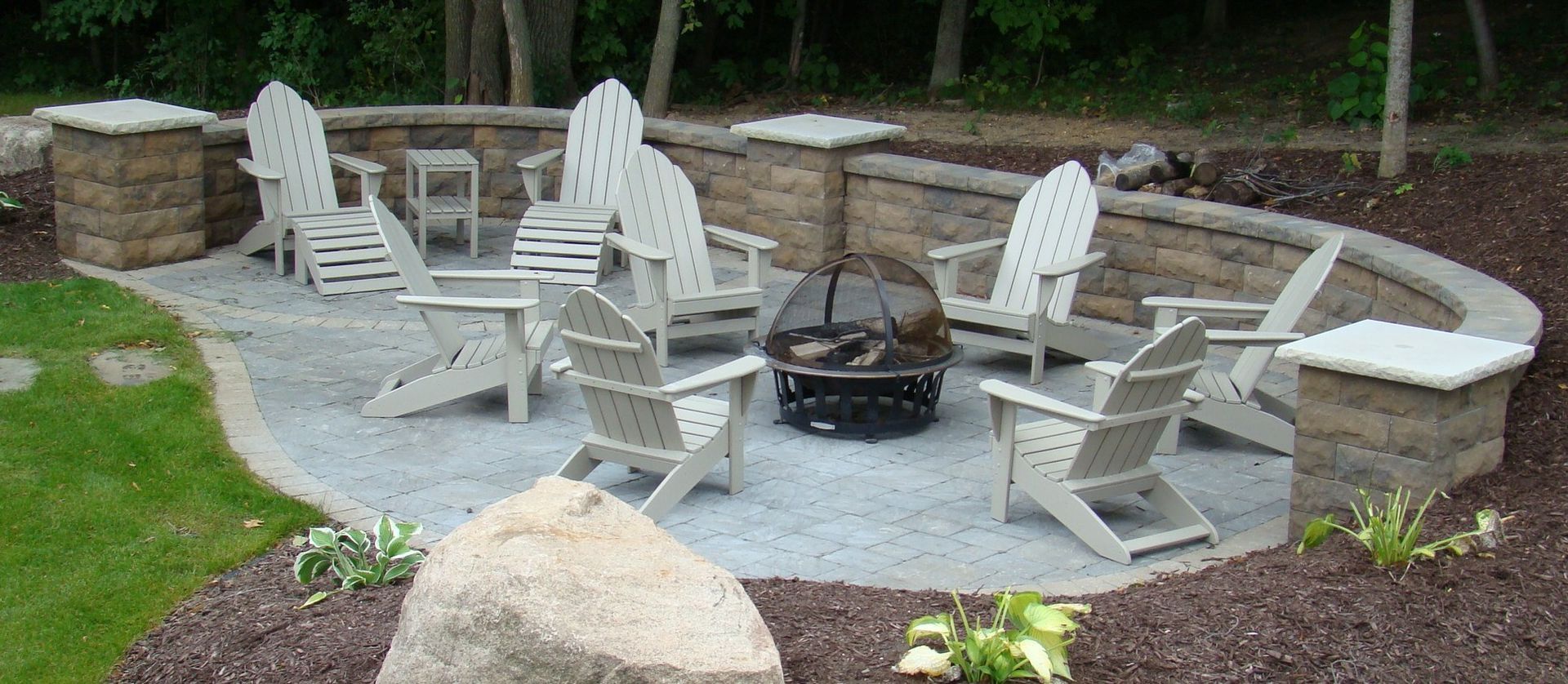 Patio with Adirondack chairs around a fire pit and a stone retaining wall.