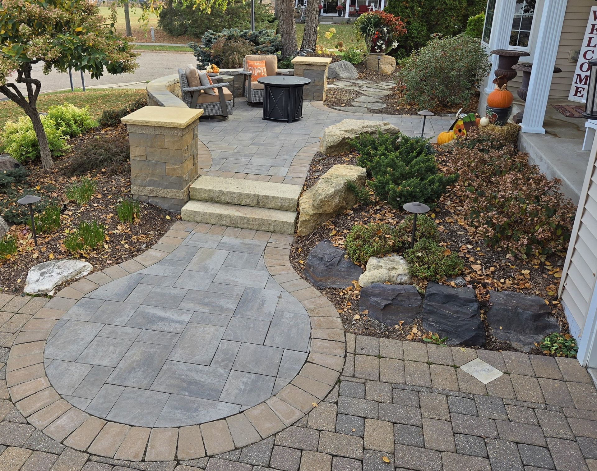 Stone pathway with steps leading to a seating area with a fire pit, surrounded by landscaping.