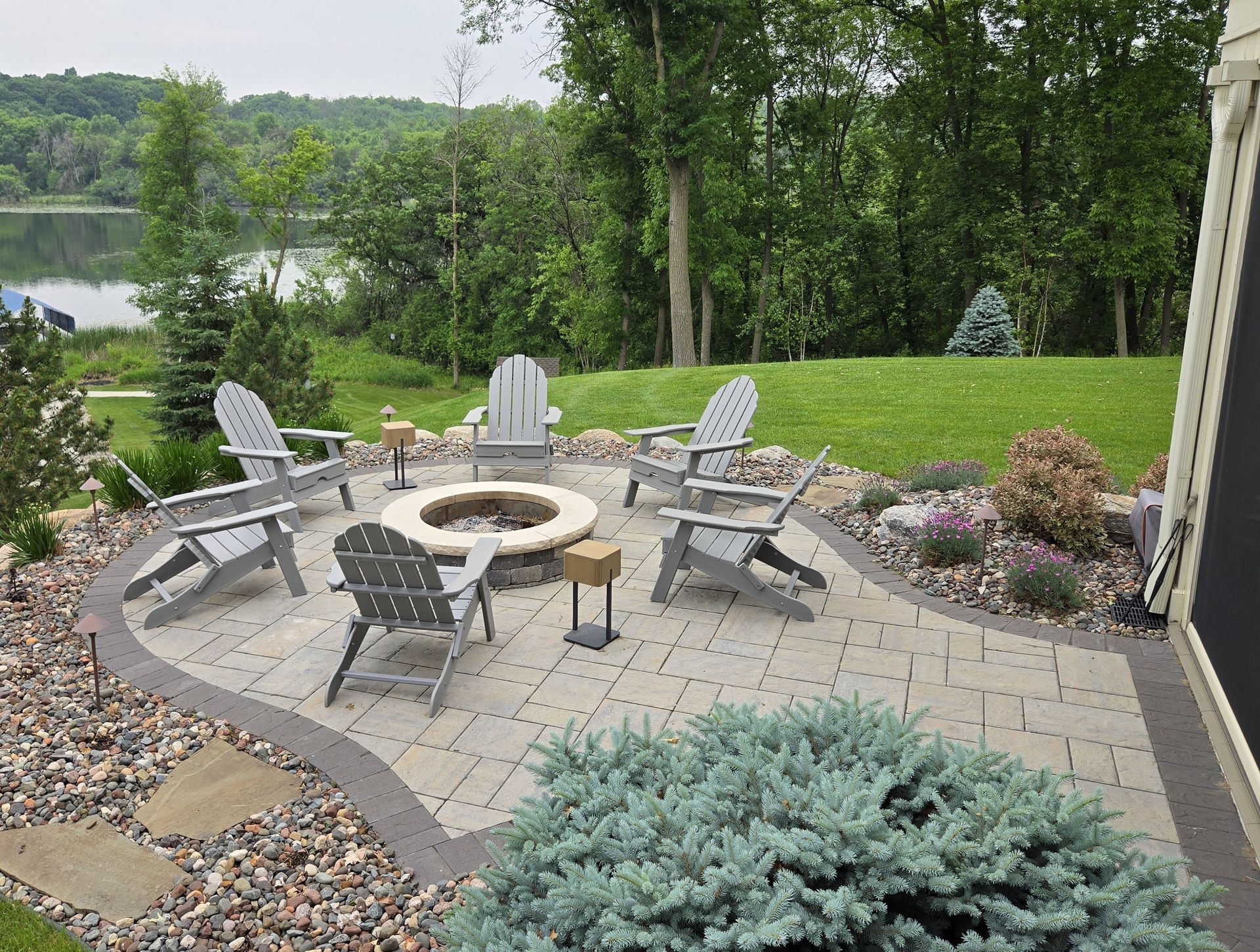 Patio with fire pit and Adirondack chairs overlooking a lake.