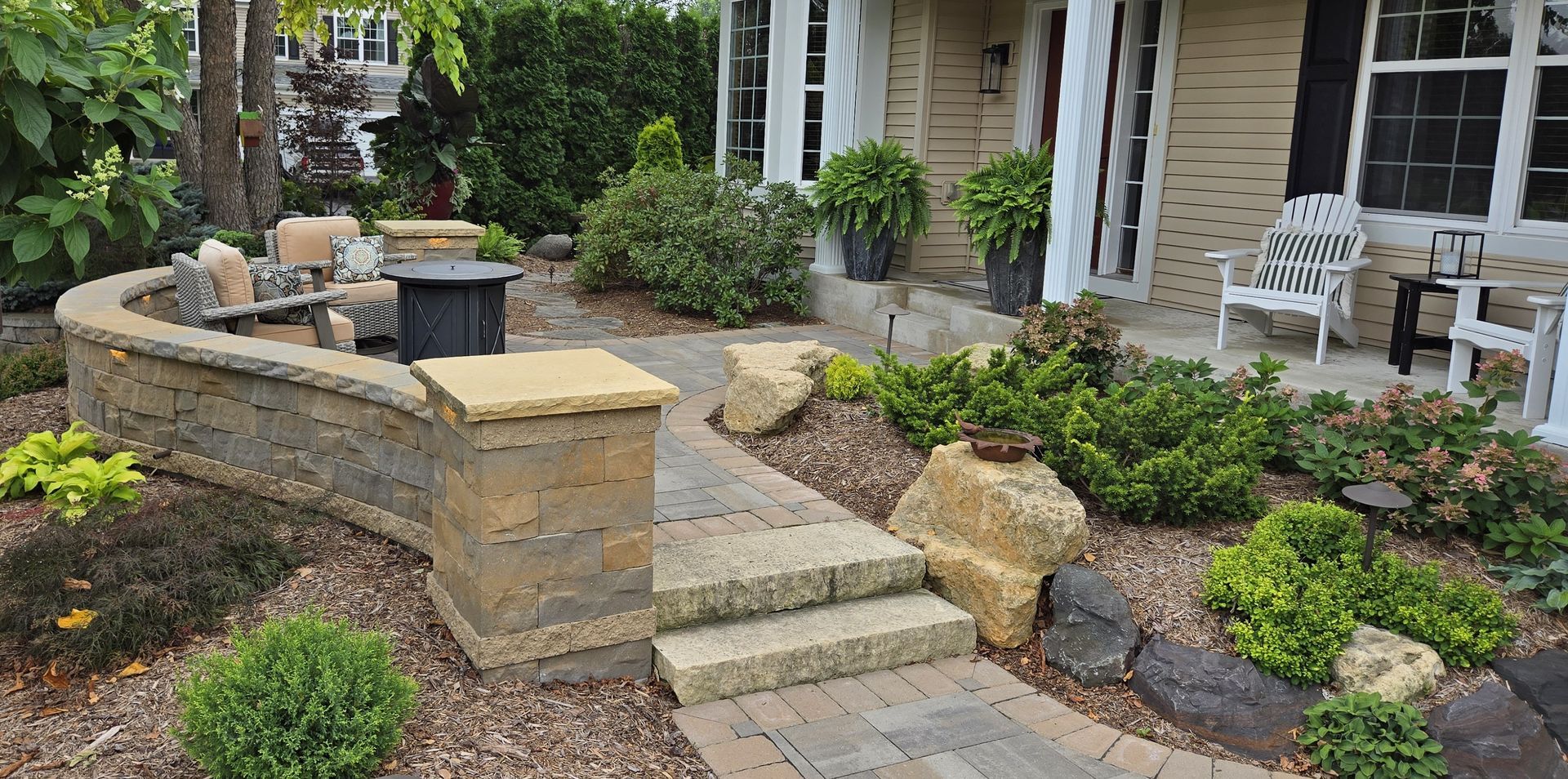 Stone walkway and landscaping in front of a house, with a curved retaining wall and steps.