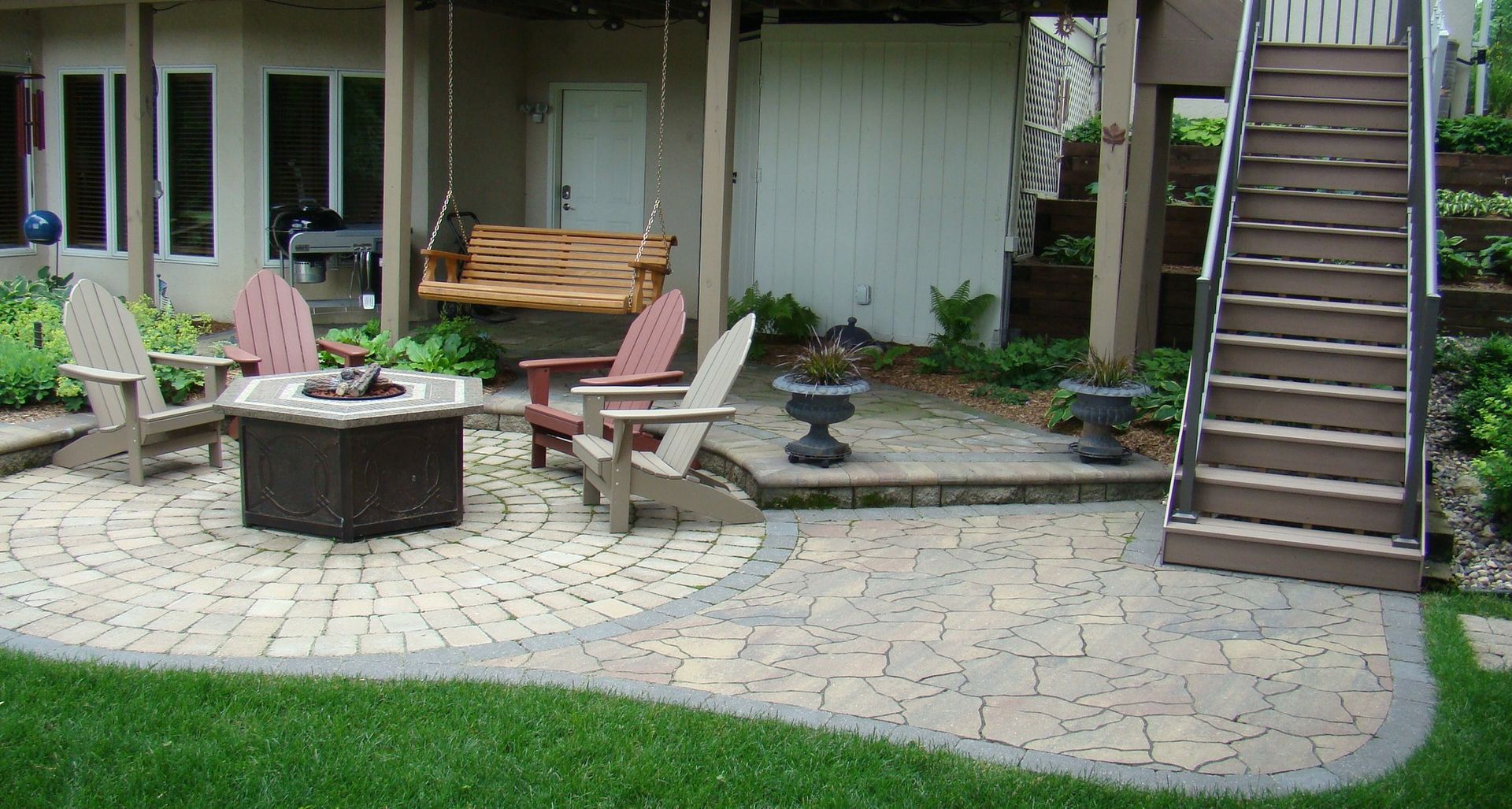 Patio with fire pit, Adirondack chairs, wooden swing, and stairs leading up.