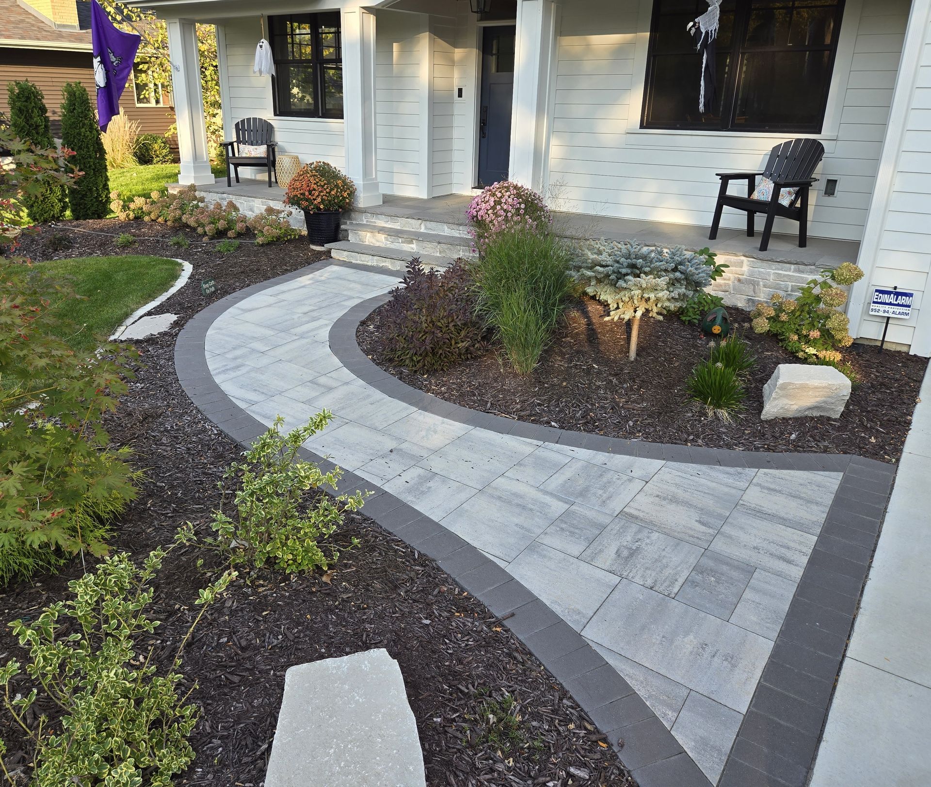 Curved paver walkway leads to a white house porch with landscaping and plants.