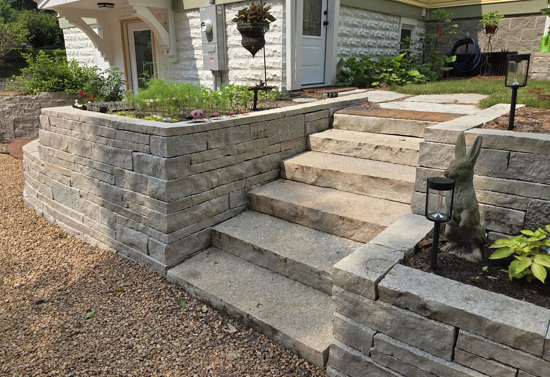 Stone retaining wall with steps leading up to a white building; gravel ground.