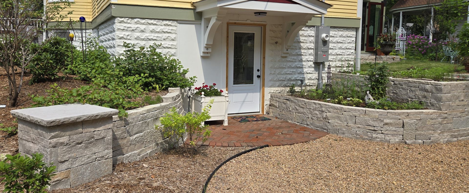 Exterior view of a house with a gravel pathway, stone walls, and a white front door.