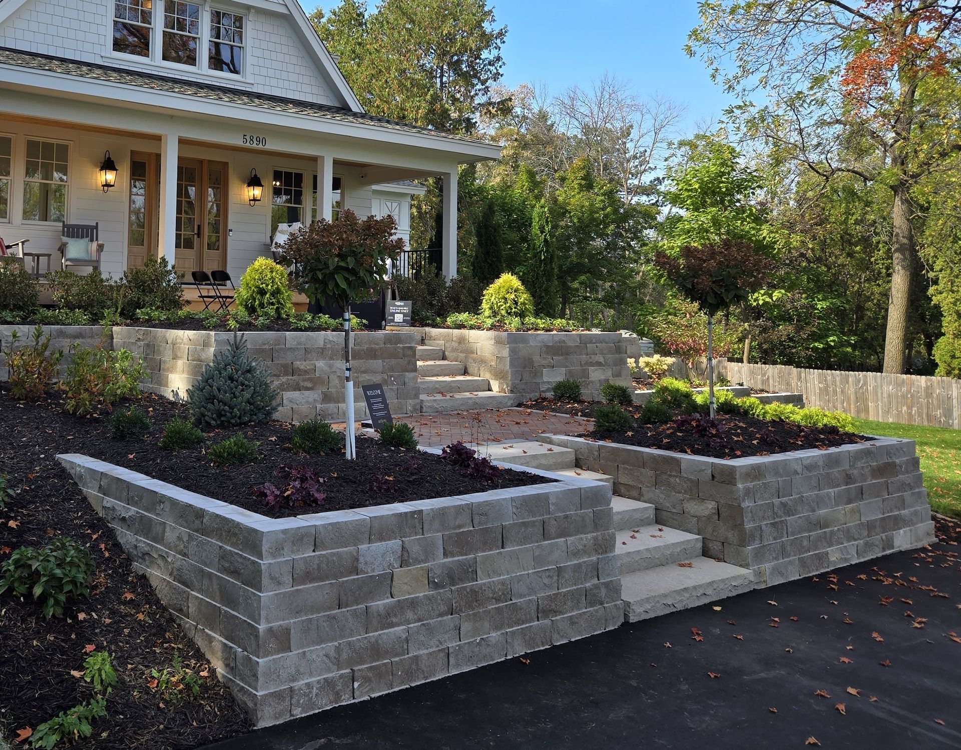 Stone retaining walls and steps leading to the porch of a white house with landscaping.