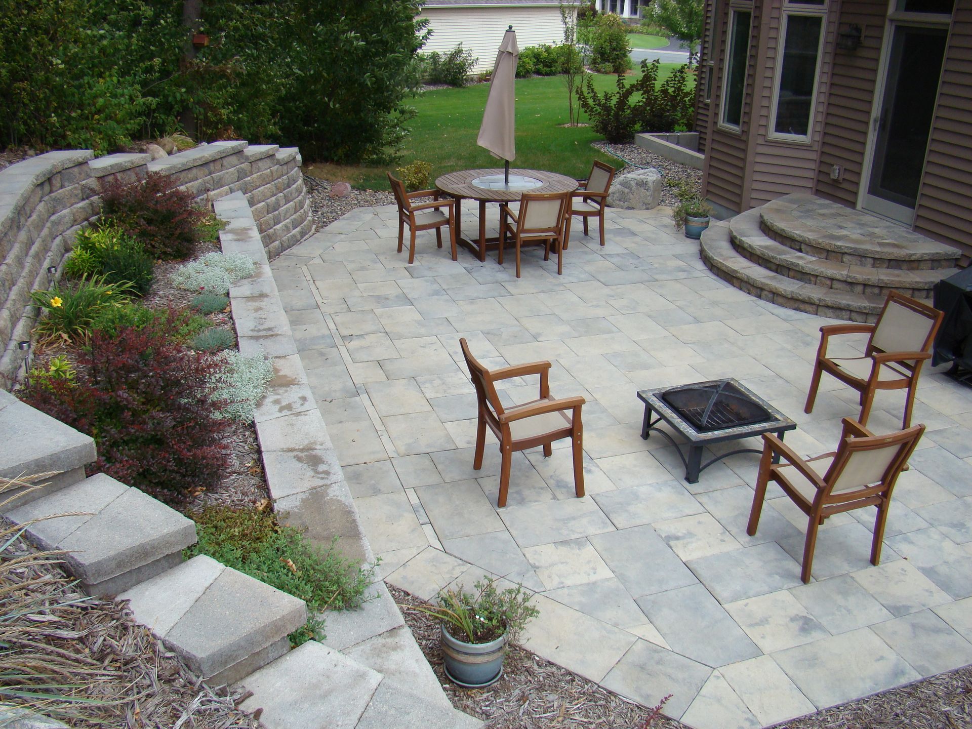 Patio with stone pavers, seating, fire pit, and tiered retaining wall with plants.
