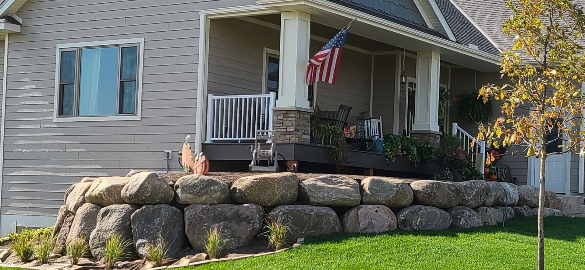 House with a stone retaining wall and an American flag hanging from the porch.