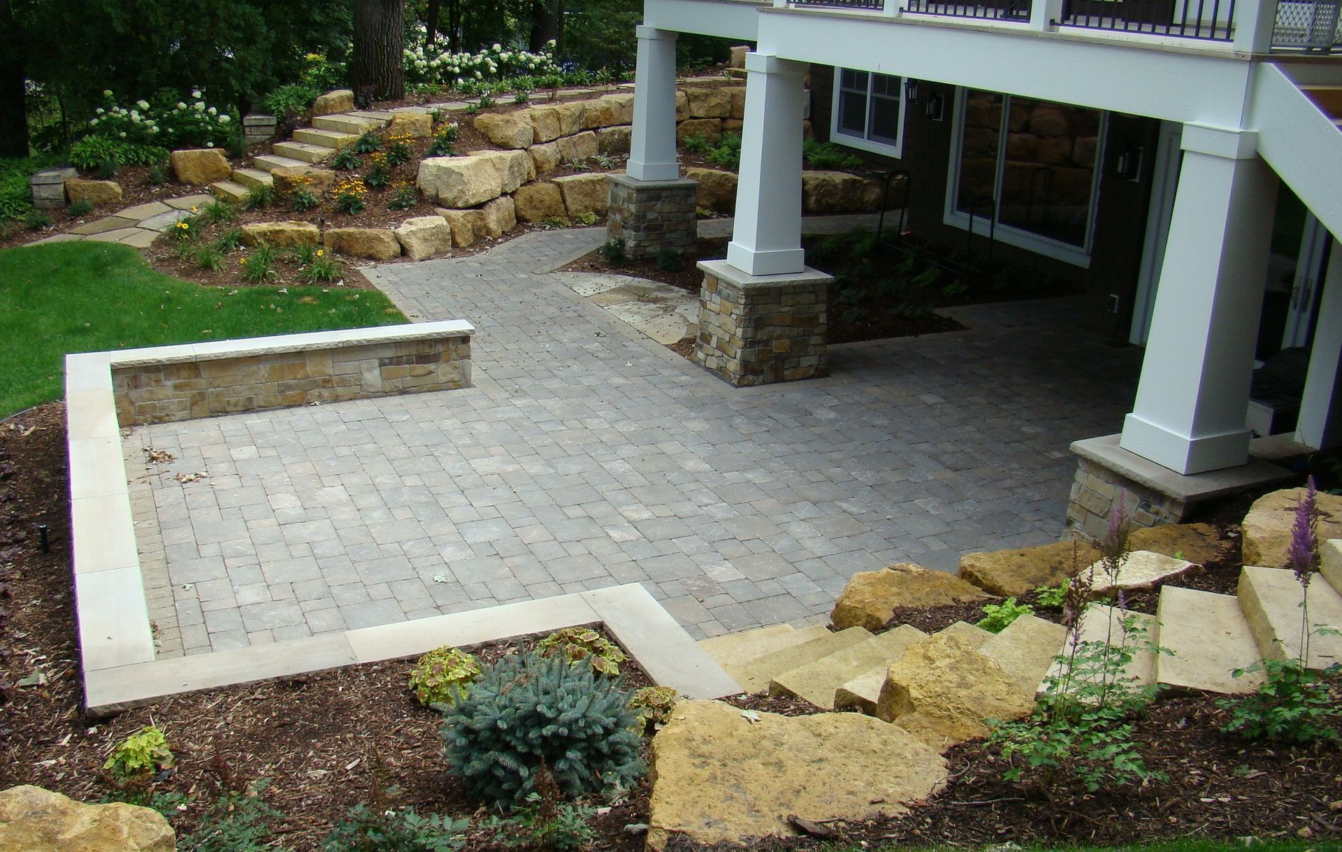 Stone patio with steps and retaining walls, leading to a house with white columns.