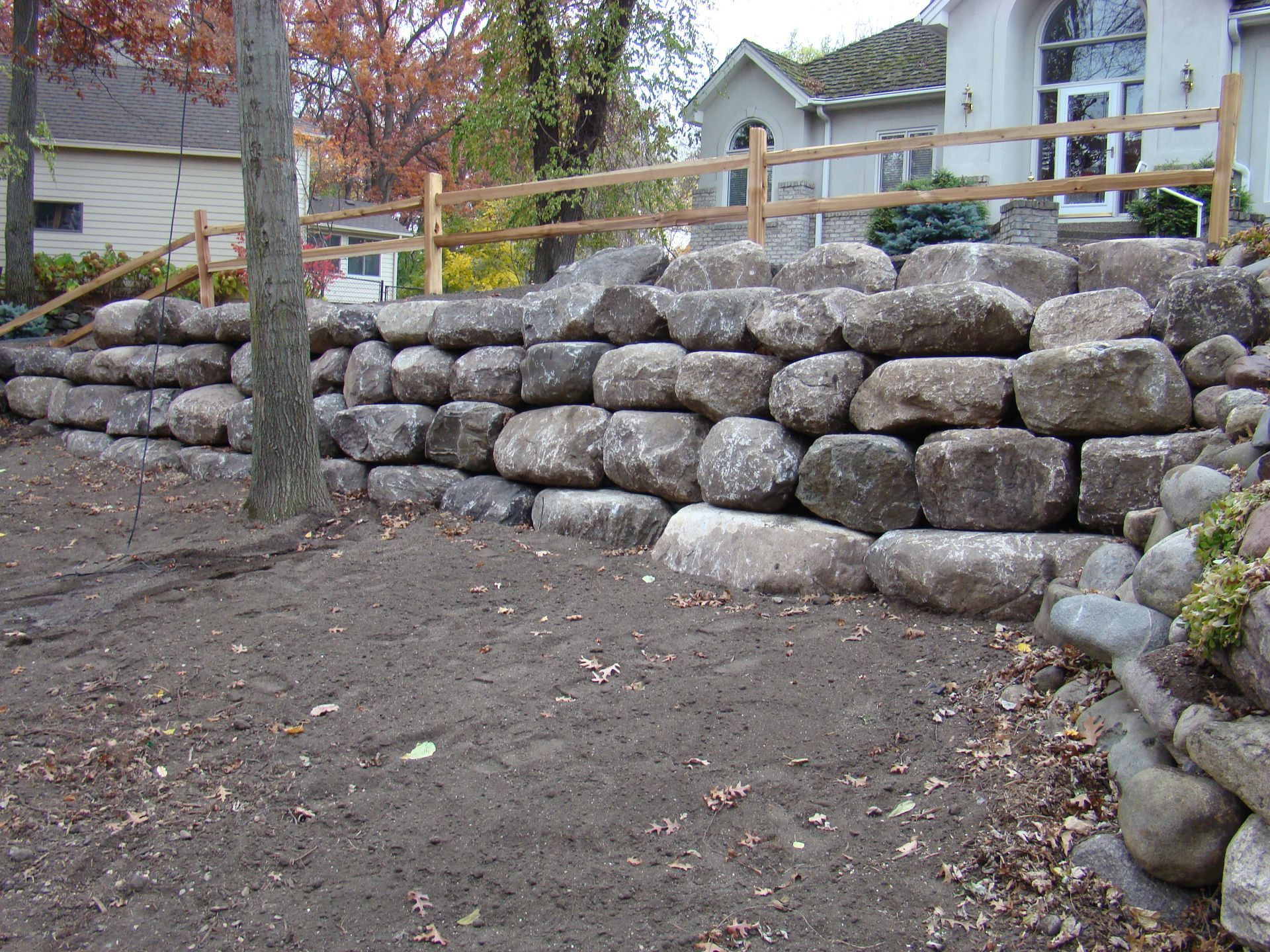 Large stone retaining wall in front of a house, with a wooden fence above.