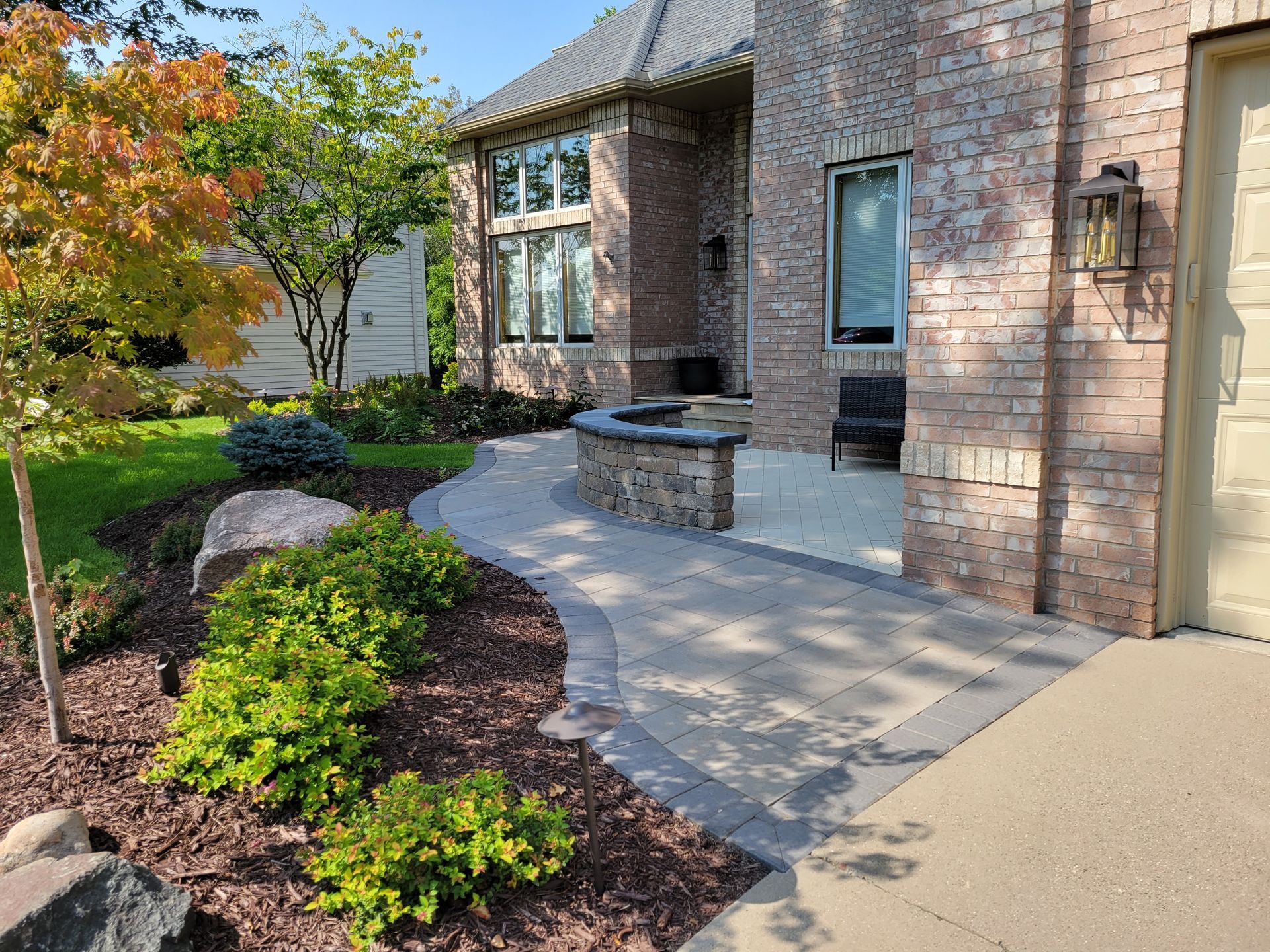 Brick house with paved walkway, landscaping, and a bench.