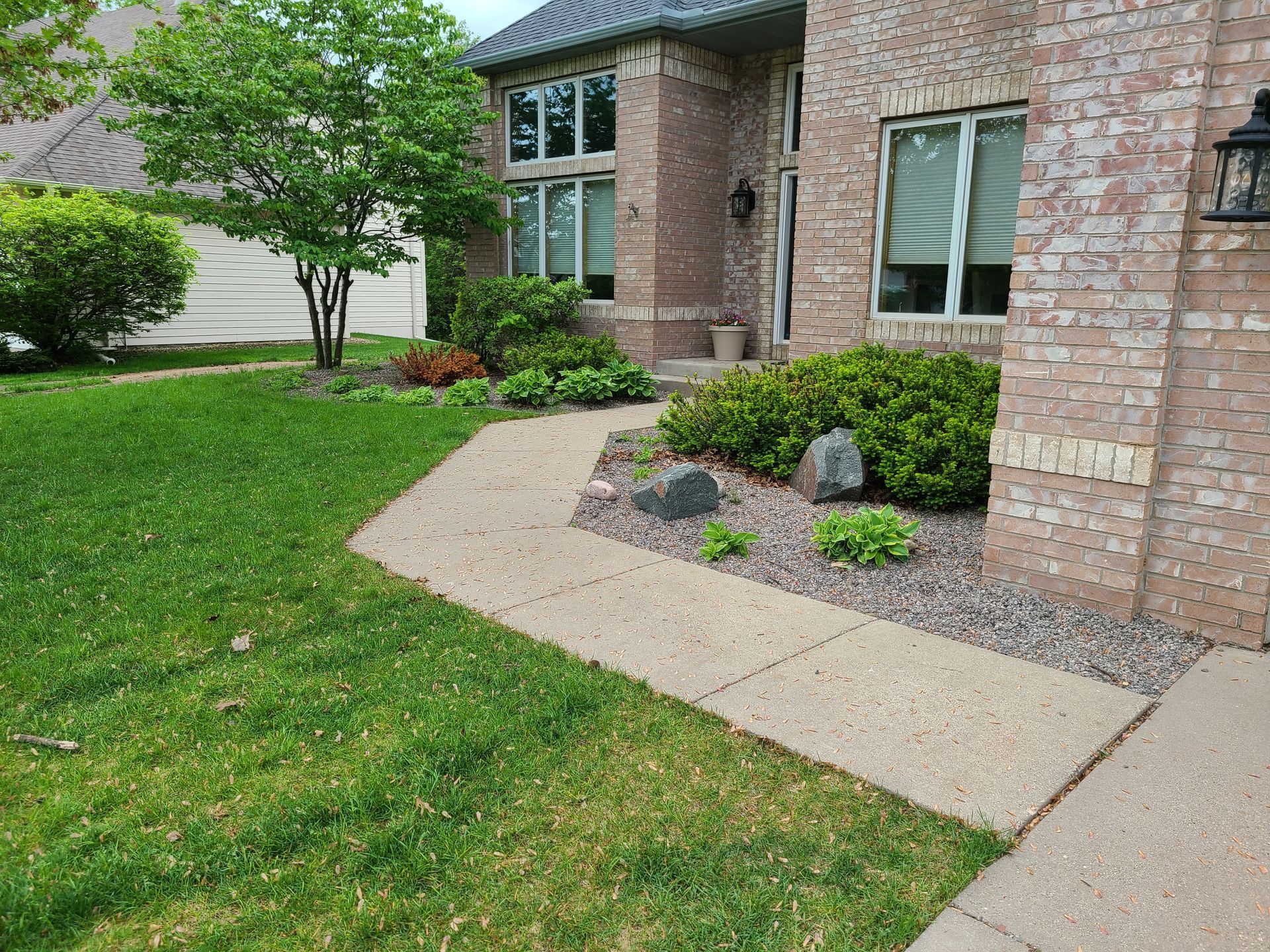 Concrete walkway leading to a brick home's entrance, surrounded by green grass and landscaping.