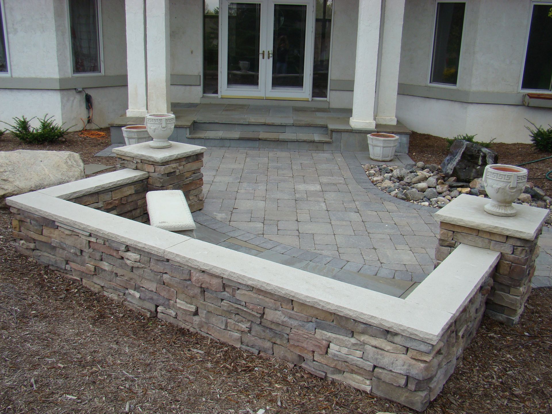 Stone retaining wall and patio leading to a home's entryway.