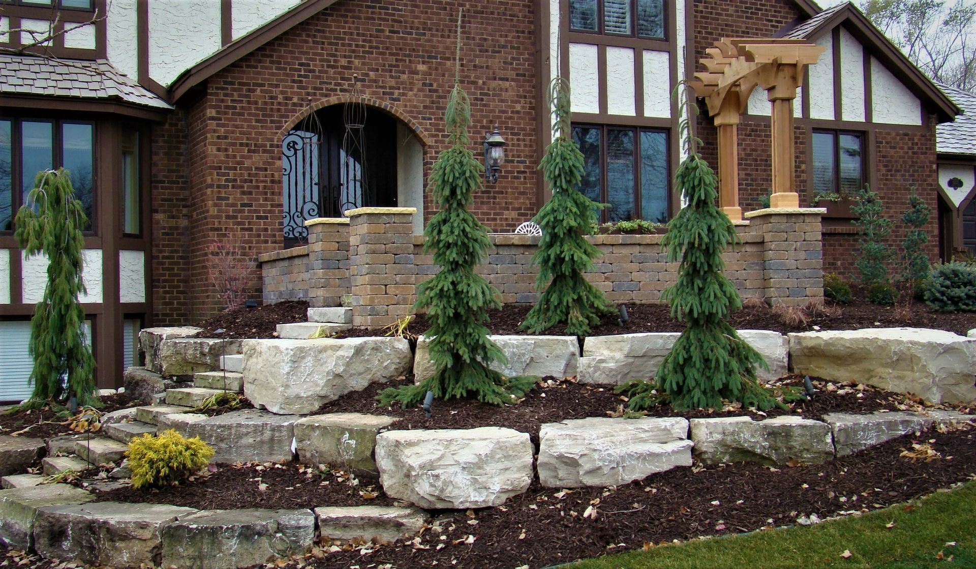 Brick home exterior with stone landscaping and young evergreen trees.