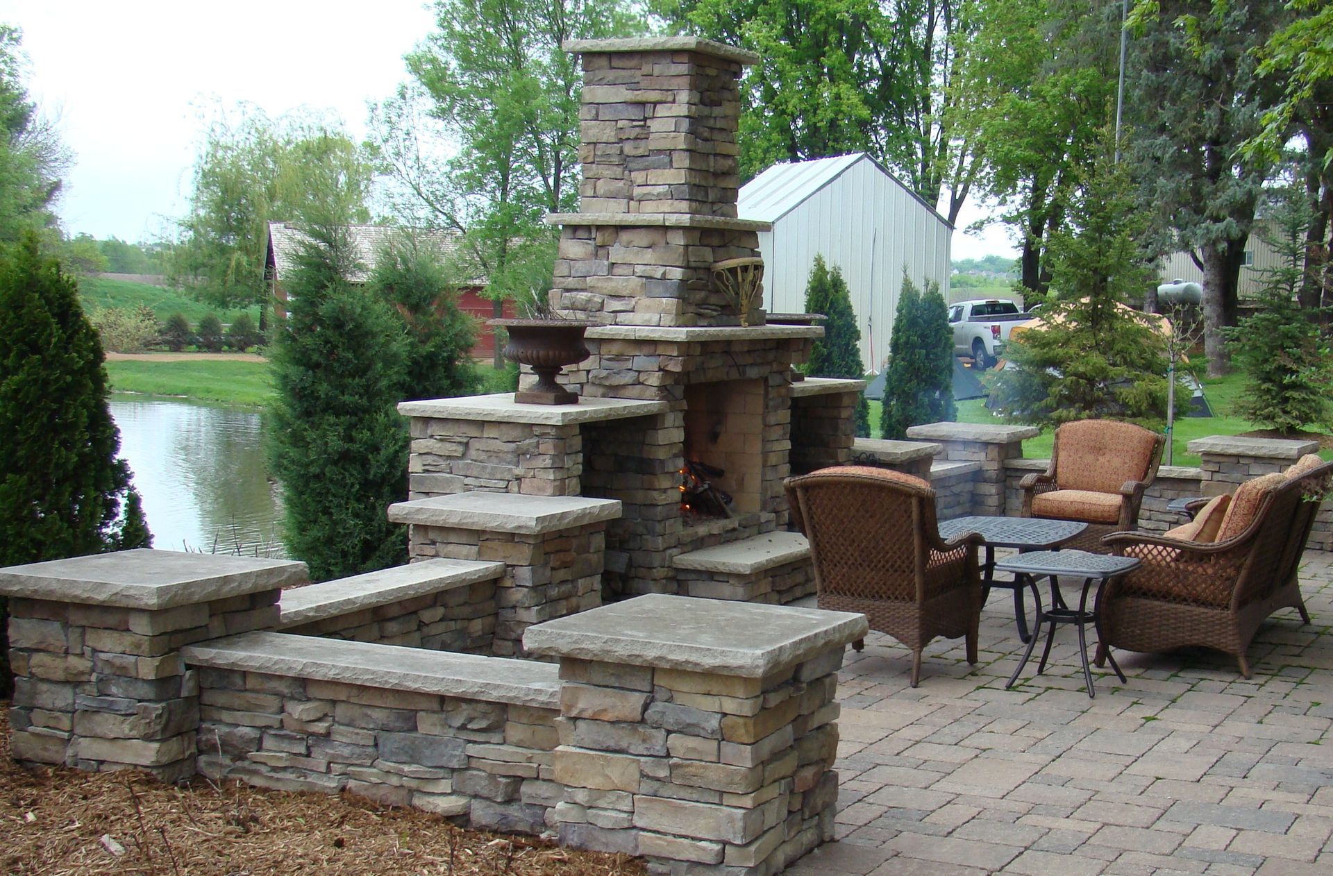 Stone fireplace and patio with seating overlooking a pond.