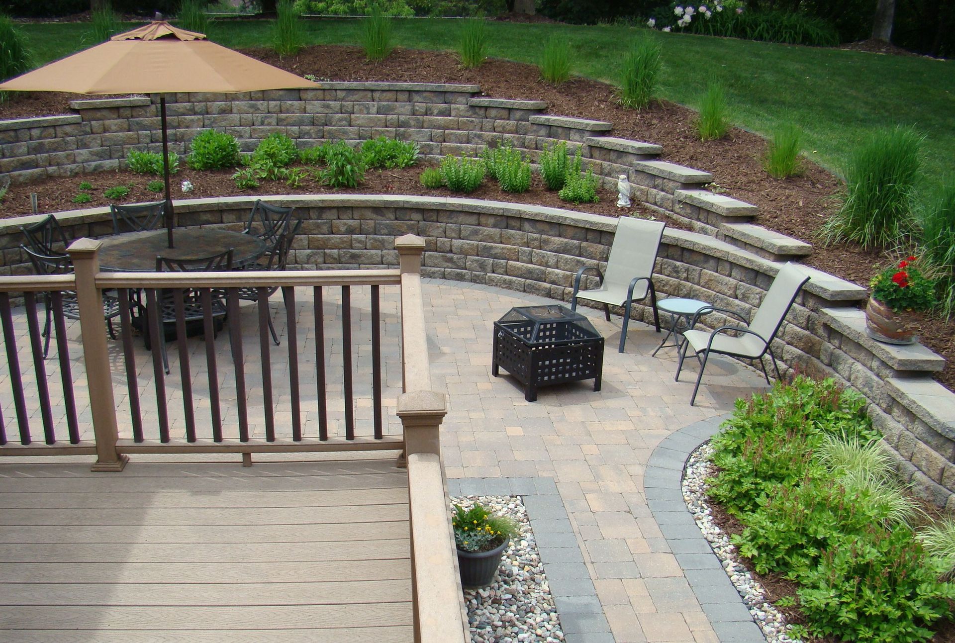Patio with tiered stone walls, deck, seating, fire pit, and landscaping.