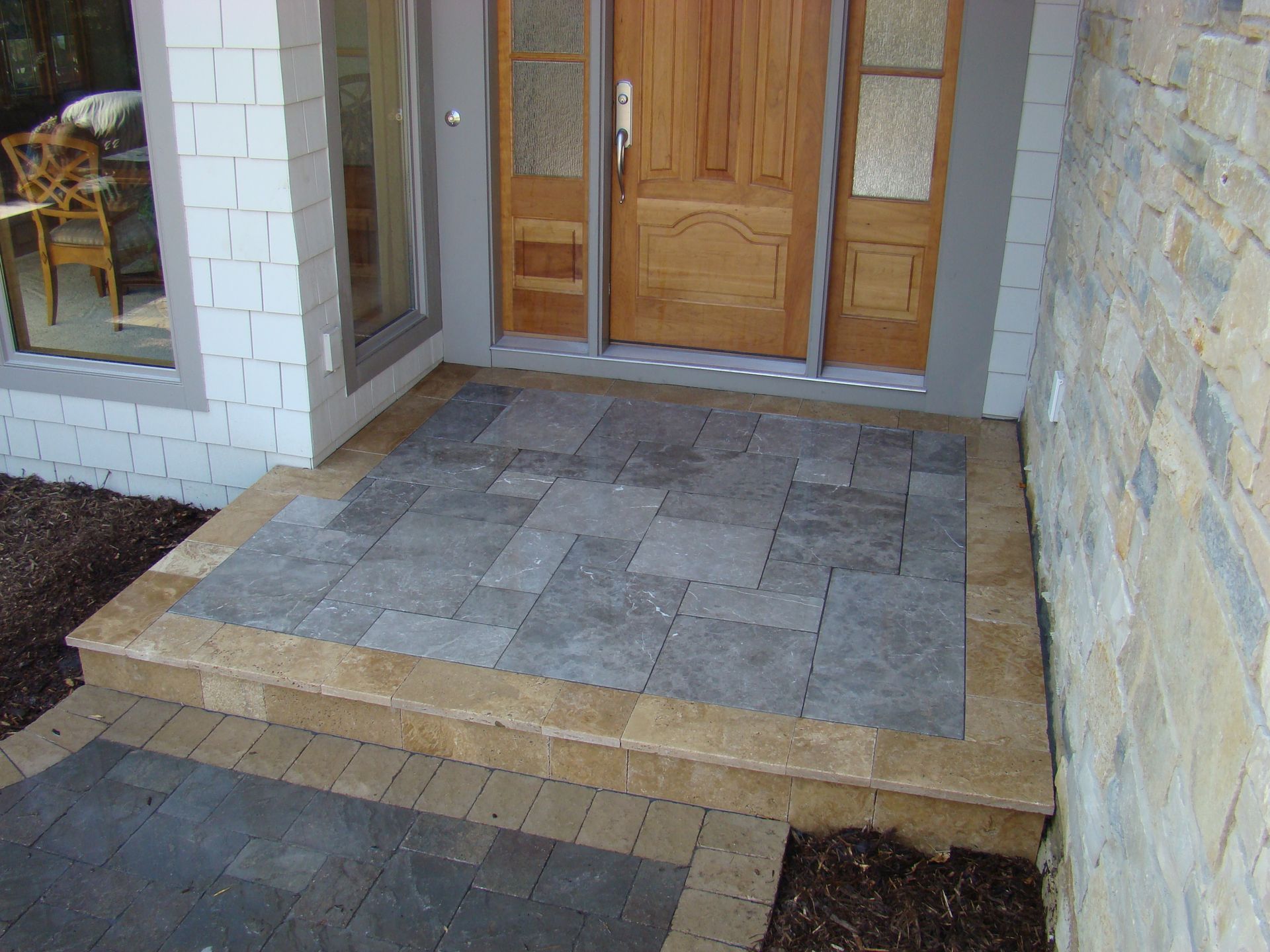 Stone front porch with wood door and gray and tan pavers.