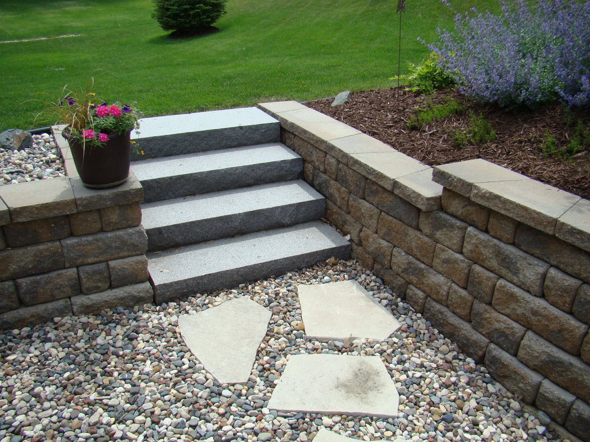 Stone steps and retaining walls in a landscaped backyard with gravel and flagstone.