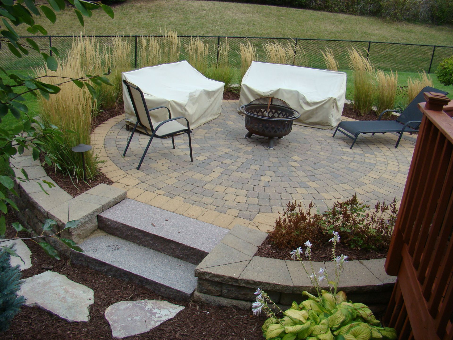 Circular patio with fire pit, covered seating, steps, and decorative landscaping.