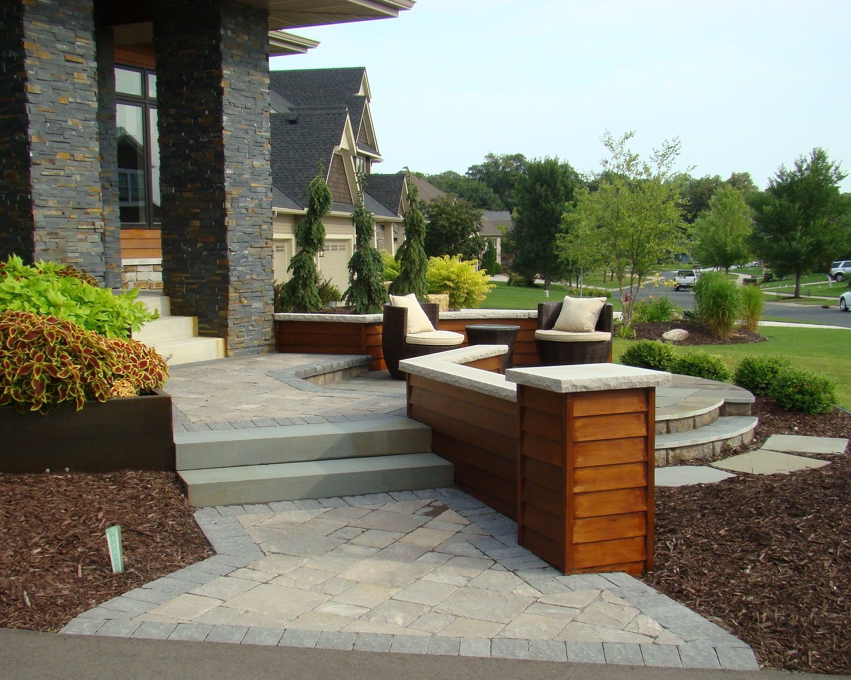 Stone patio with built-in seating, wooden accents, and a front entry to a house.