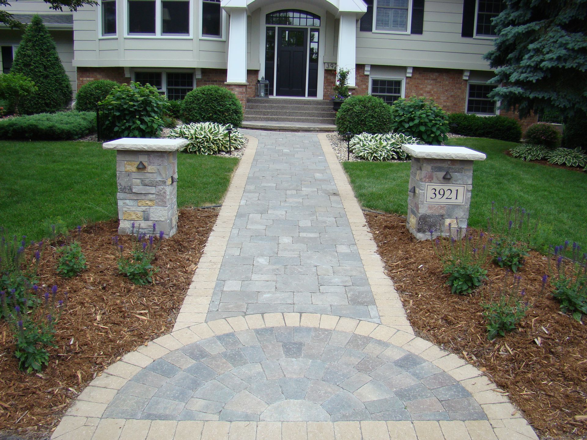 Stone pathway leading to a house with pillars, address numbers, and landscaping.