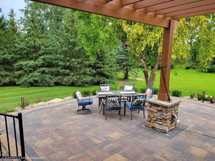 Patio with dining set under a pergola, overlooking a green lawn with trees.