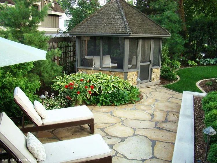 Patio with flagstone, lounge chairs, screened gazebo, and lush landscaping.