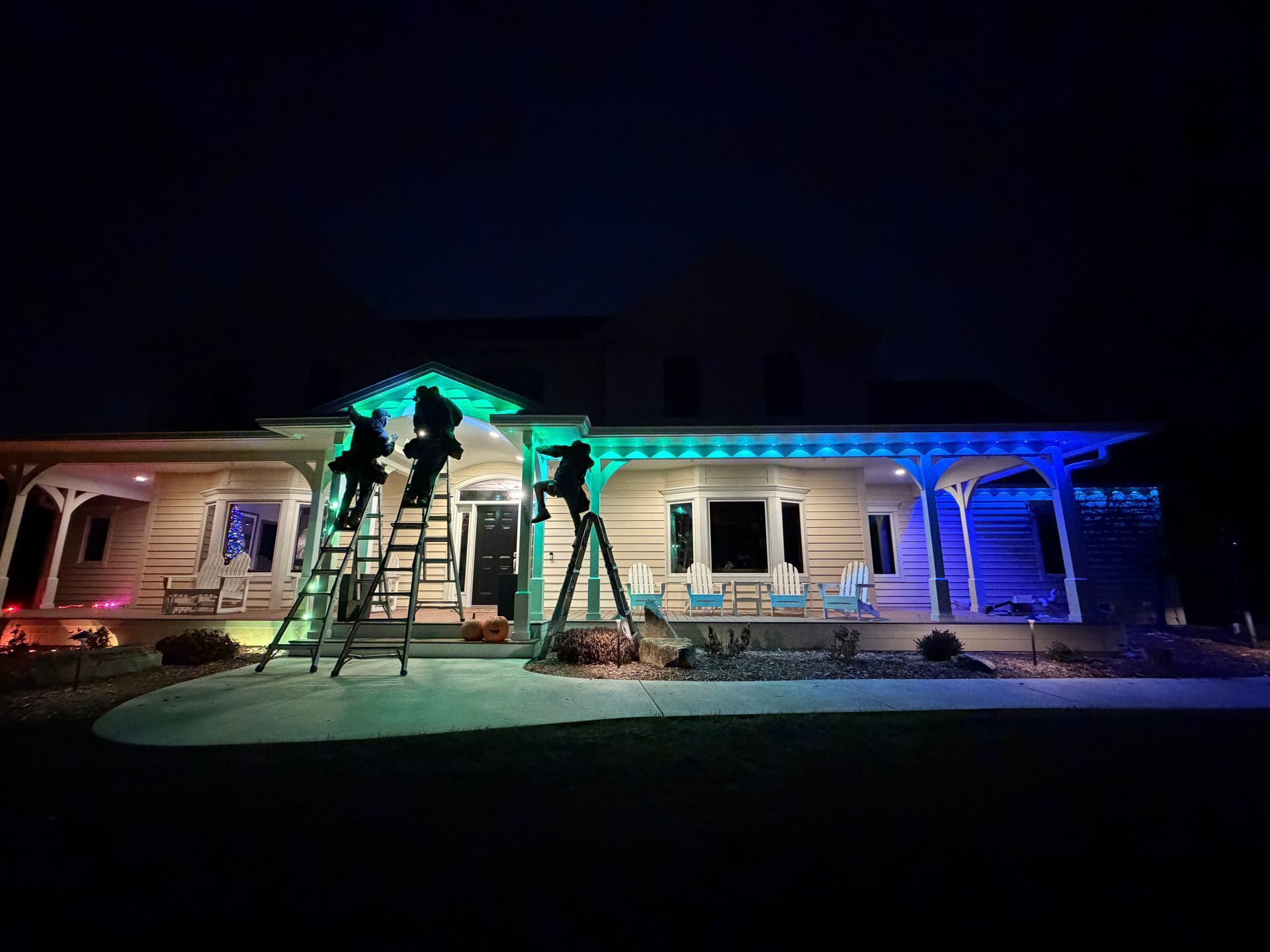 Home decorated with colorful lights, people on ladders, setting up decorations at night.