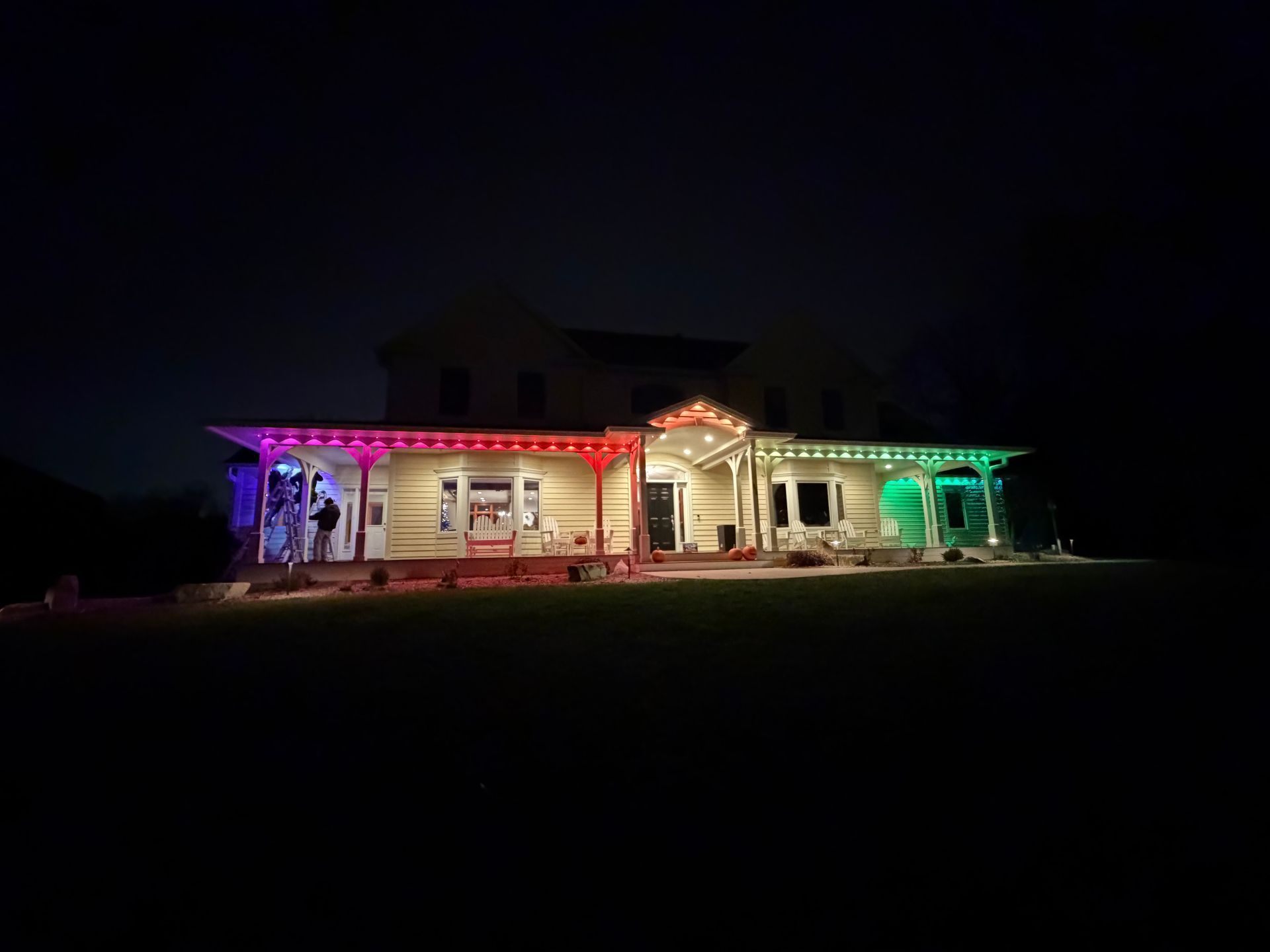 House at night with porch lights in red, white and green.