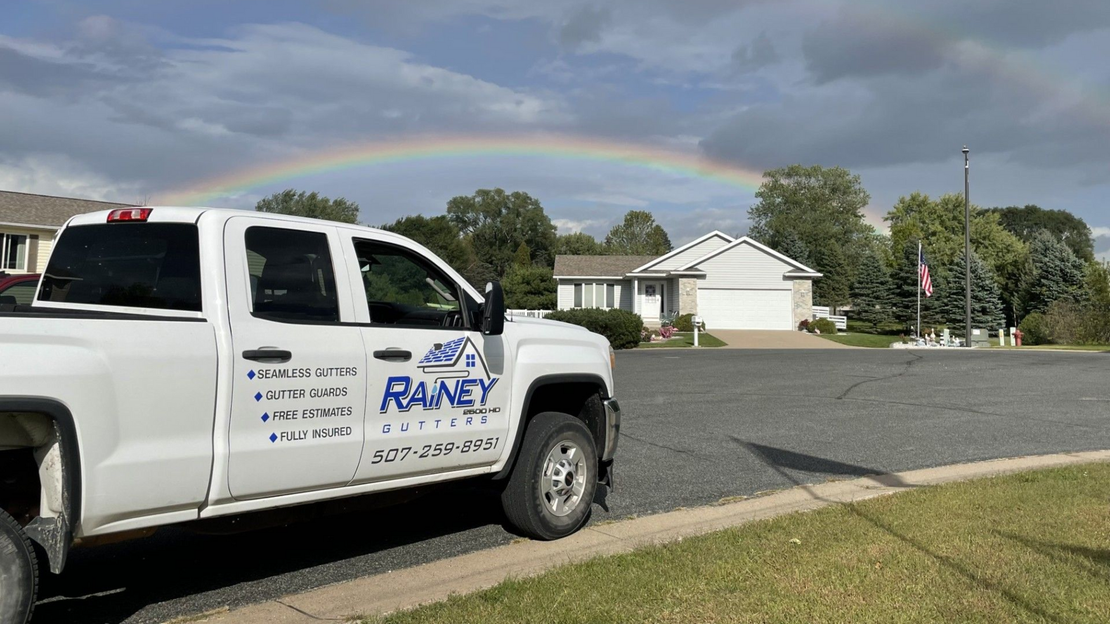 White truck parked on a street with a rainbow arching over a suburban house.