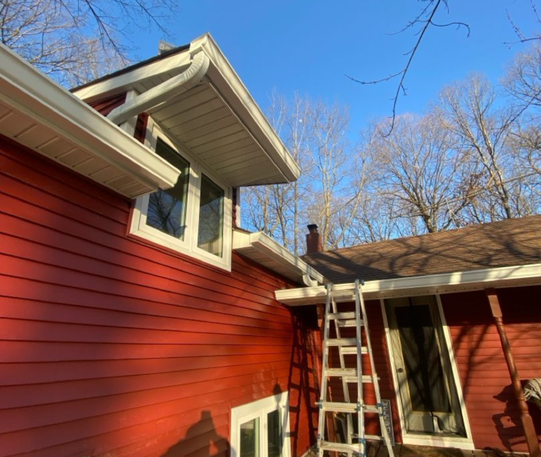 Red house with white trim; ladder leans against roof. Sunny day.