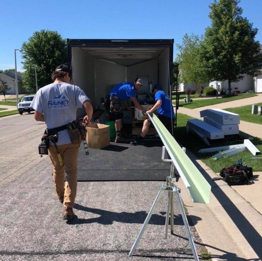 Three people unloading gutter materials from a trailer on a residential street. One man walks away.