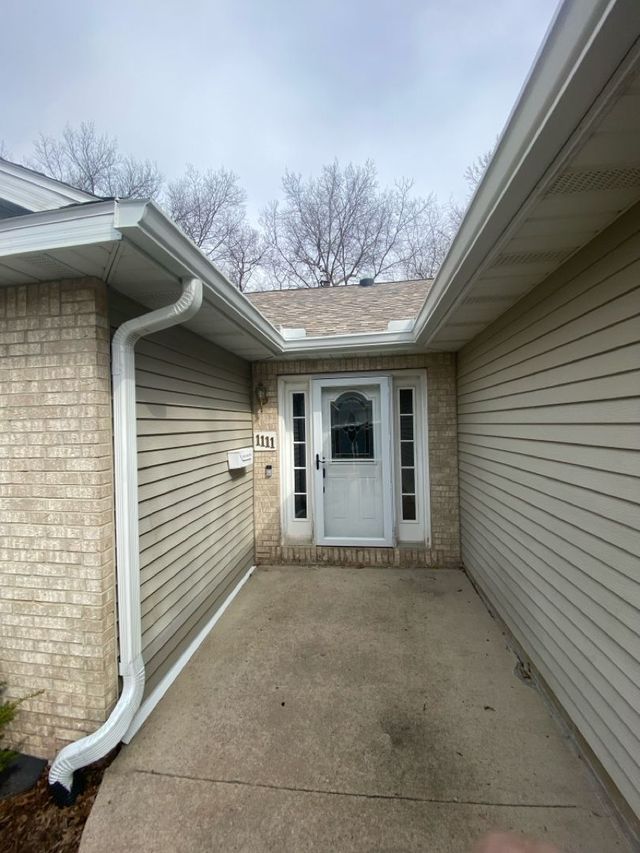 Exterior view of a house with white door, siding, brick, and concrete walkway under a cloudy sky.