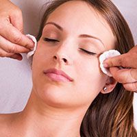 A woman is getting her face cleaned with cotton swabs.