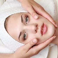 A woman with a towel wrapped around her head is getting a facial treatment.