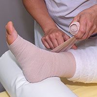 A person is bandaging a person 's ankle with a bandage.