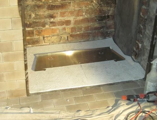 Fireplace under construction, showing brick and plaster walls, with a new hearth installed.