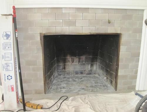 Fireplace with light gray tiled surround, dark interior, and tools nearby.