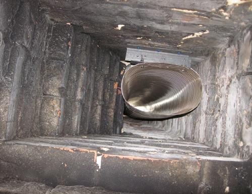Looking up a chimney, a silver vent pipe is visible in a dark, brick-lined shaft.
