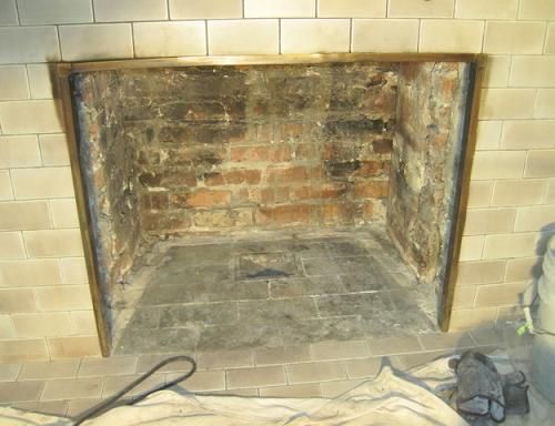 Empty brick fireplace with gray tiled floor and brass frame, surrounded by light-colored tile.