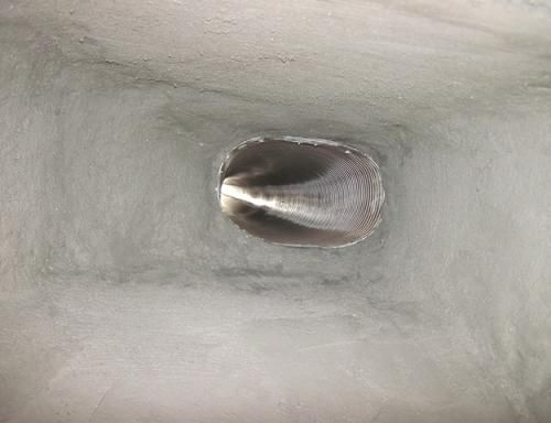 Inside view of a metallic tube with a central oval-shaped opening, reflecting light. The inner surface is textured.