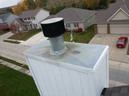 White chimney with black cap on a residential rooftop.
