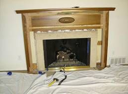 Fireplace with a wood mantel, light-colored stone surround, and dark firebox; a drop cloth lies below.