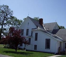 White house with multiple gabled roofs, several windows, and a brick chimney under a blue sky.