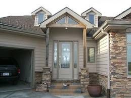 Beige house with a covered entry, stone columns, and a garage; a car is visible.